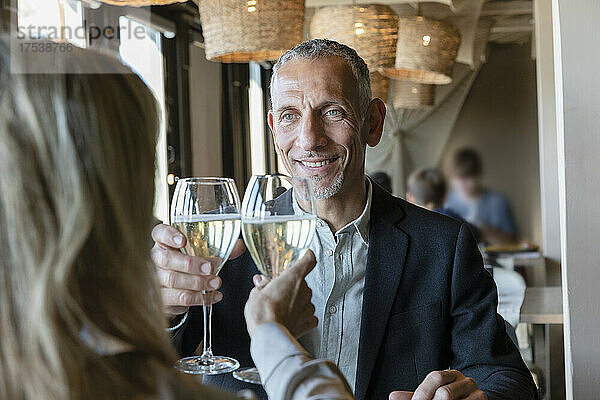 Lächelnder Mann prostet beim Mittagessen im Restaurant mit einer Frau ein Glas Champagner an