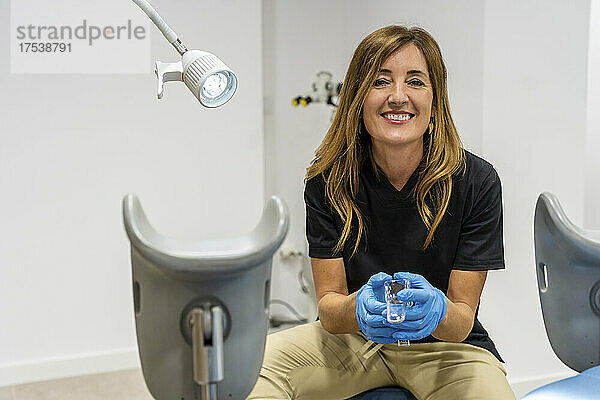 Smiling gynecologist wearing protective gloves sitting in clinic