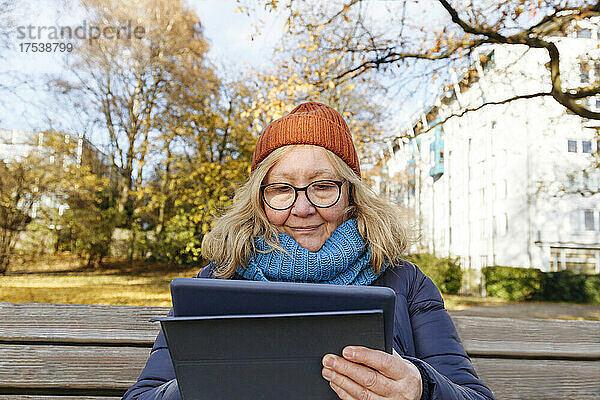 Senior woman using tablet PC sitting on bench in park