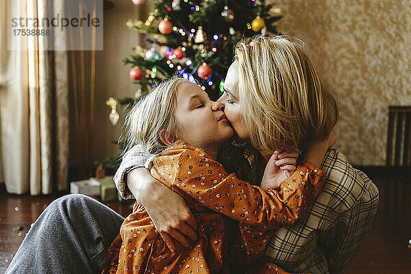 Mutter küsst Tochter zu Hause vor dem Weihnachtsbaum