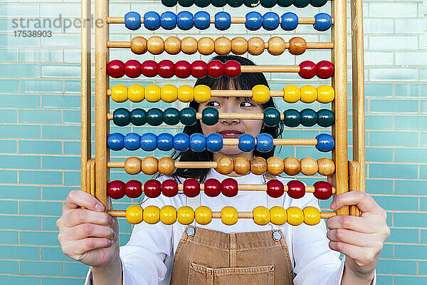 Young woman holding multi colored abacus in front of brick wall