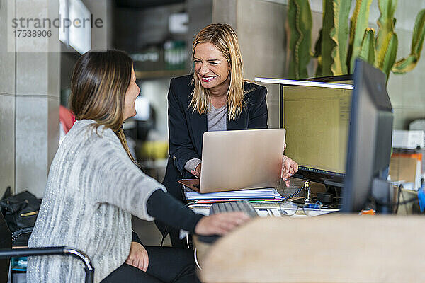 Fröhliche Geschäftsfrau mit Laptop blickt auf Kollegen im Büro