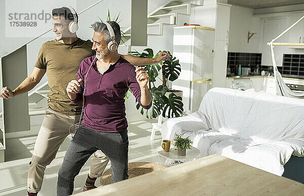 Playful gay couple listening music dancing together in living room at home