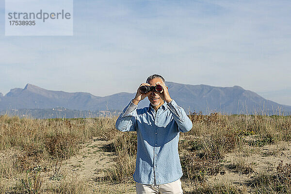 Mann schaut durch ein Fernglas und steht in der Wüste