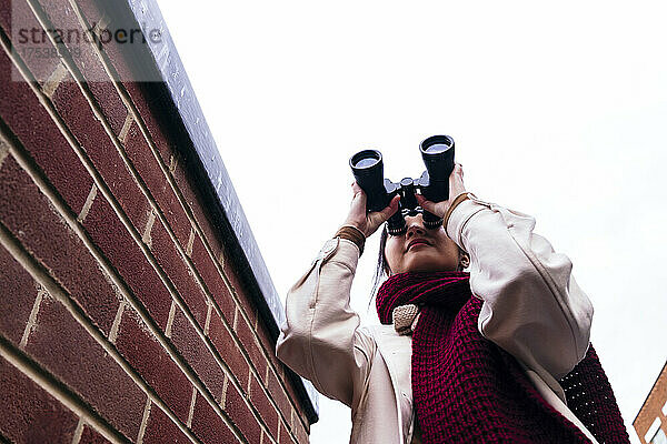 Young woman wearing scarf looking through binoculars