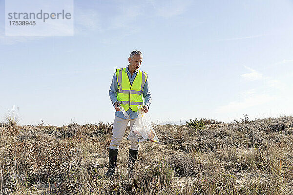 Mann sammelt Plastikflaschen aus Sanddünen ein