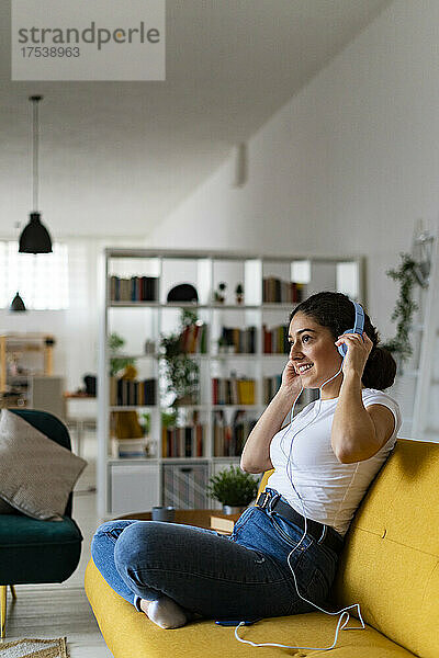 Smiling woman adjusting wired headphones at home