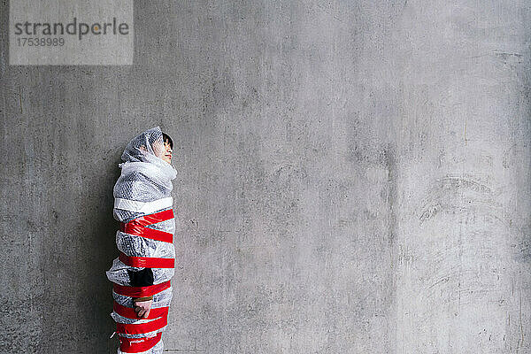 Woman in bubble wrap leaning on gray wall
