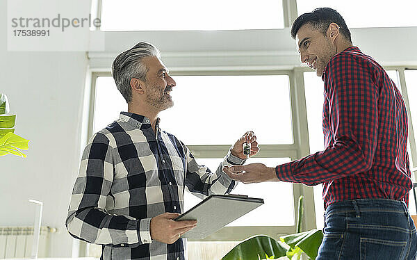 Smiling real estate agent giving key to buyer at home