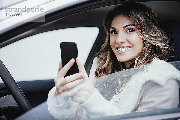 Young woman holding smart phone in car