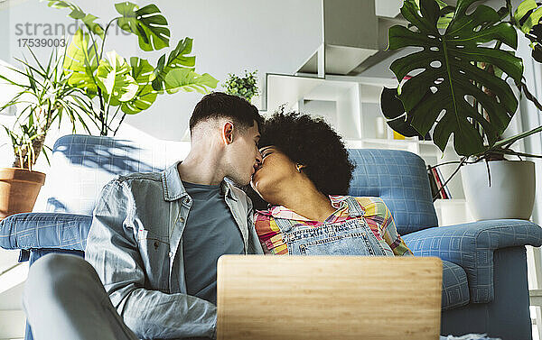 Junges Paar küsst sich mit Laptop im Wohnzimmer auf den Mund
