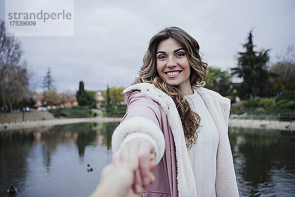 Lächelnde Frau hält die Hand eines Freundes am Seeufer
