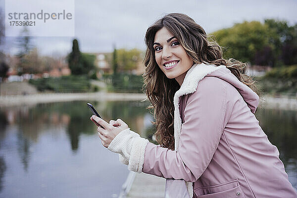 Smiling woman holding mobile phone on pier