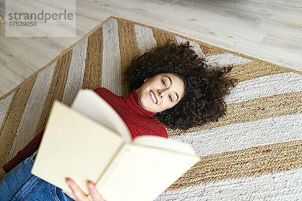 Young woman with book lying on carpet at home