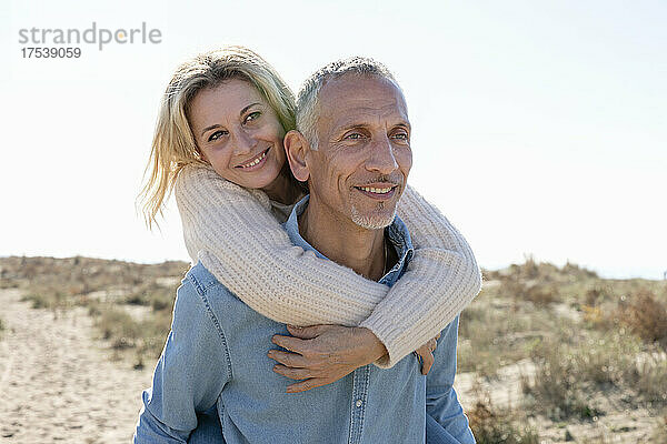 Smiling woman embracing man on sand dunes