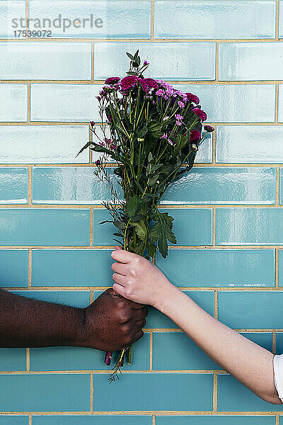 Man and woman holding bouquet on turquoise brick wall