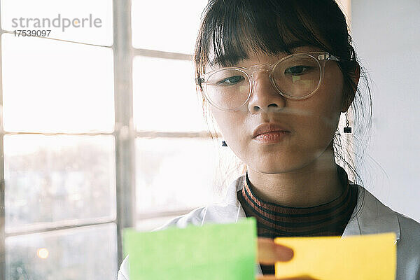 Young chemist sticking adhesive note on glass in laboratory