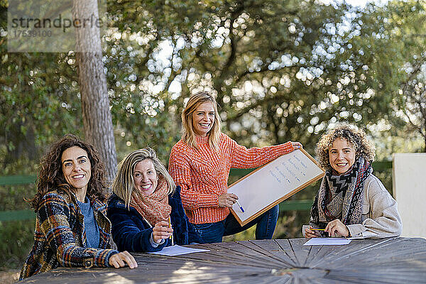 Smiling woman holding whiteboard by friends at park