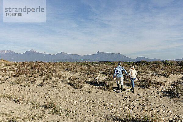 Paar spaziert gemeinsam zwischen Pflanzen im Sand der Dünen