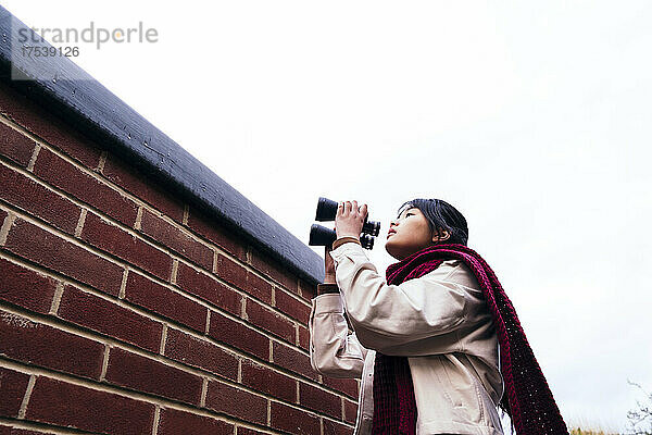 Woman holding binoculars standing near brick wall