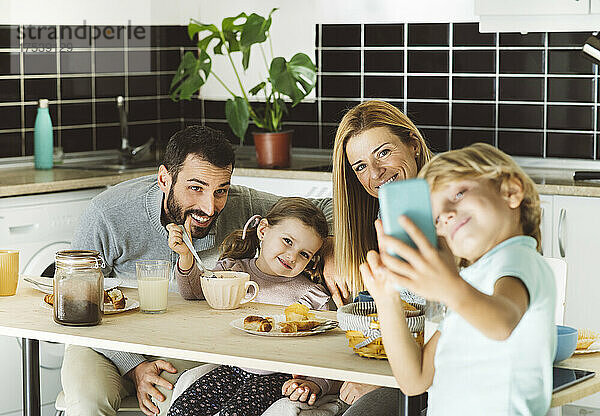 Junge macht Selfie mit glücklicher Familie am Frühstückstisch