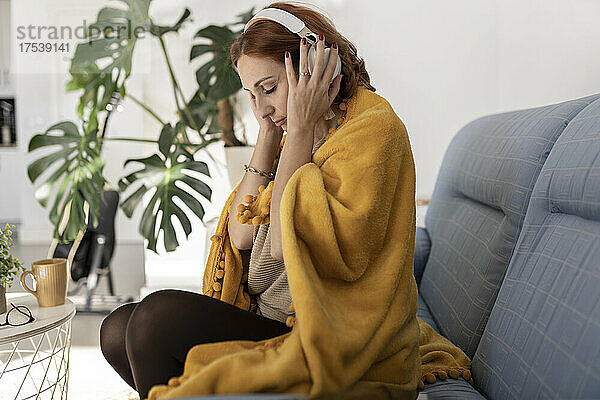 Frau mit geschlossenen Augen hört zu Hause Musik über Kopfhörer