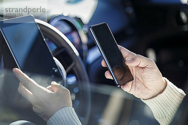 Die Hände eines Mannes halten Mobiltelefon und Tablet-PC im Auto