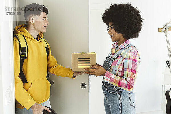 Young man delivering package to smiling woman at doorway