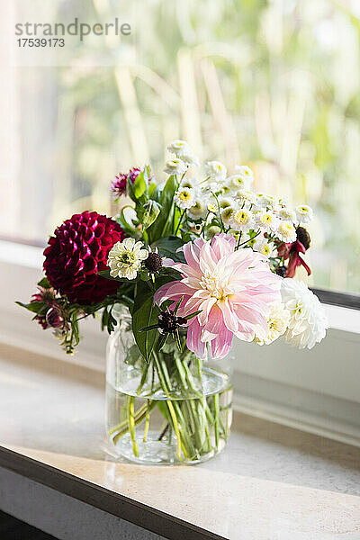 Glas mit bunten Blumen steht auf der Fensterbank