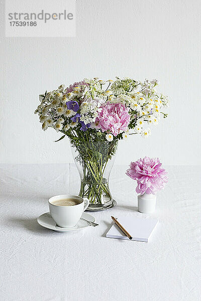 Studioaufnahme einer Tasse Kaffee und eines Straußes aus Pfingstrosen  Mutterkraut (Tanacetum parthenium)  Glockenblumen (Campanula) und weißen Spitzenblumen (Orlaya grandiflora)
