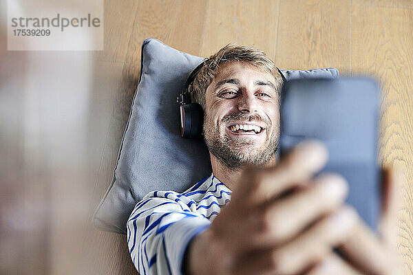 Happy man with headphones taking selfie on smart phone at home