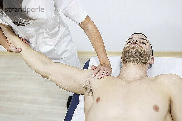 Physical therapist stretching sportsman's hand on massage table