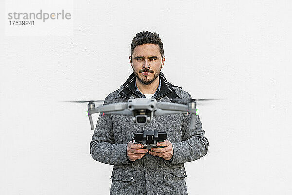 Confident man flying drone against white background