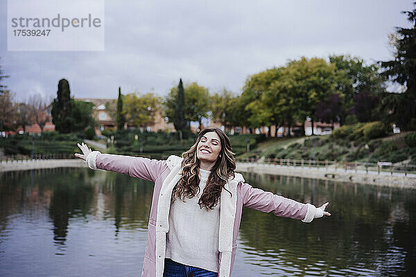 Smiling young woman with arms outstretched at lakeside