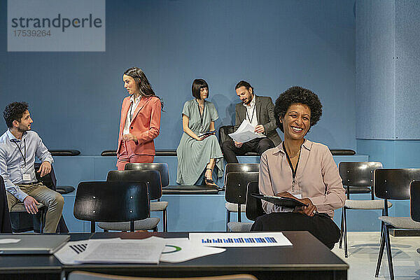 Glückliche Geschäftsfrau mit Kollegen  die im Hintergrund im Büro diskutieren
