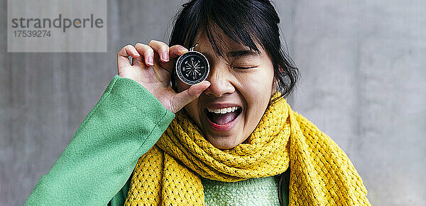 Cheerful woman covering eye with compass