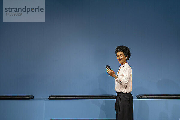 Lächelnde Geschäftsfrau benutzt Mobiltelefon am Arbeitsplatz