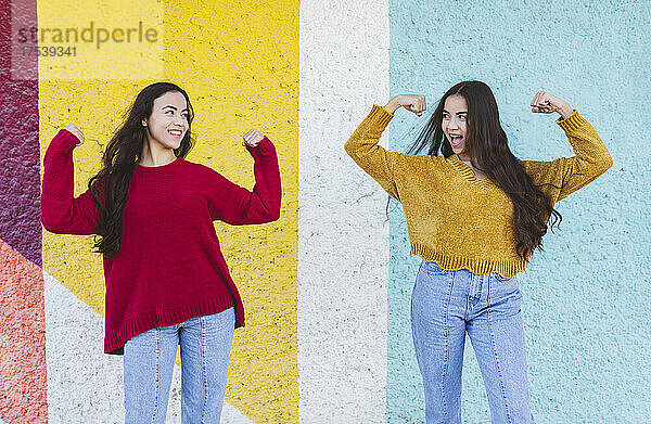 Smiling sisters flexing muscles in front of multi colored wall