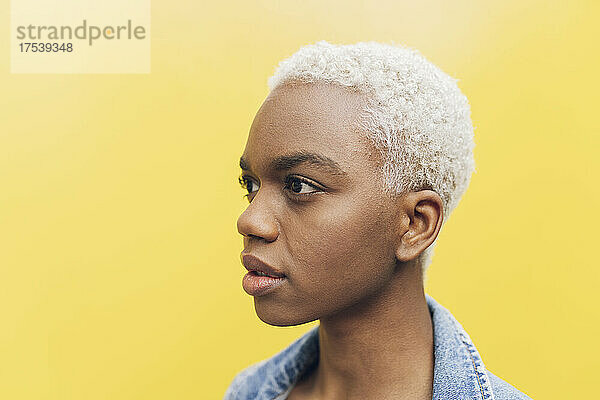 Contemplative woman with short blond hair against yellow background