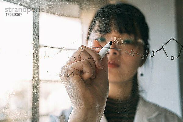 Young scientist writing on transparent glass in laboratory