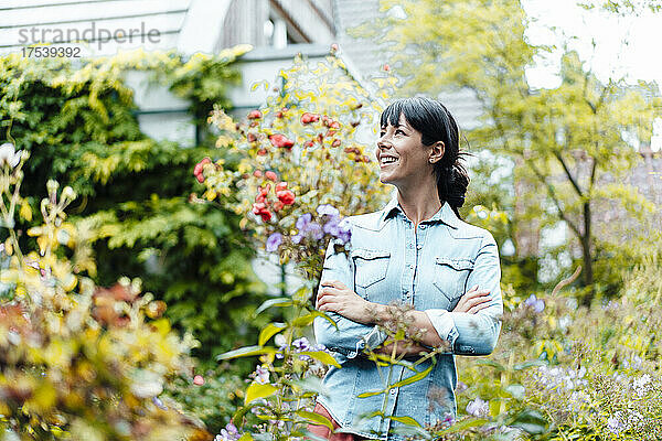 Happy woman with arms crossed standing amidst plants