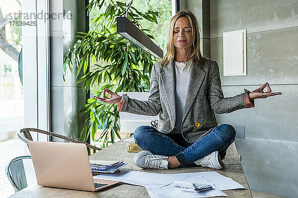 Geschäftsfrau praktiziert Yoga am Tisch im Büro