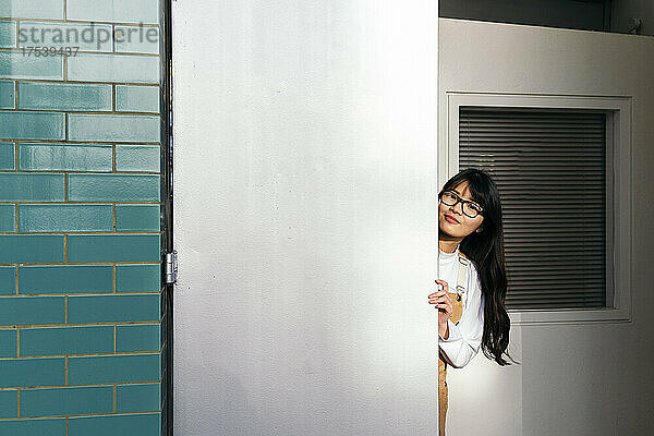 Young woman peeking from behind white door