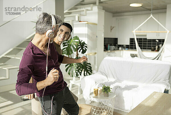 Gay couple listening music through headphones and dancing at home