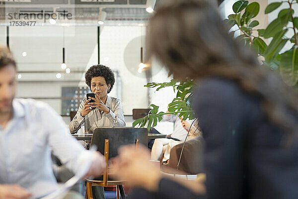 Geschäftsfrau nutzt Mobiltelefon und Kollegen diskutieren im Büro