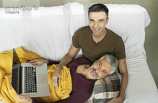 Smiling gay couple with laptop on sofa at home
