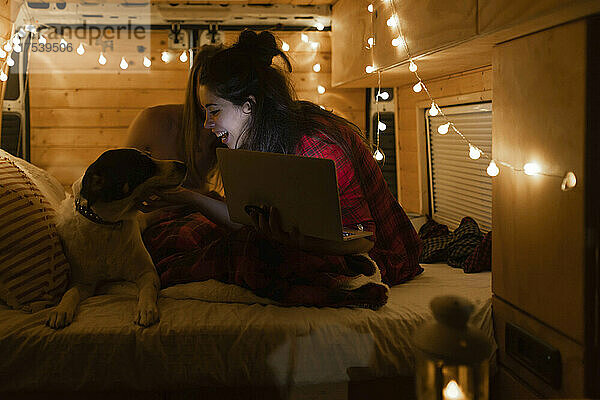 Happy woman with laptop looking at dog in illuminated van