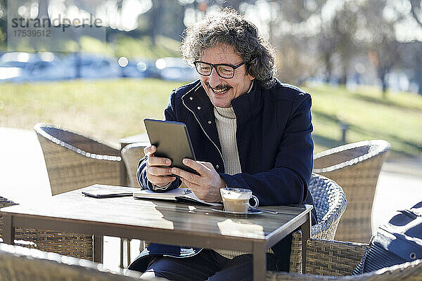 Happy man on video call using tablet PC sitting at sidewalk cafe