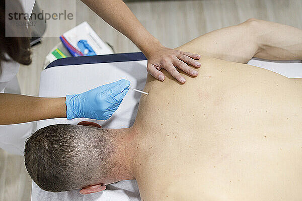 Physical therapist applying acupuncture needle on athlete's back