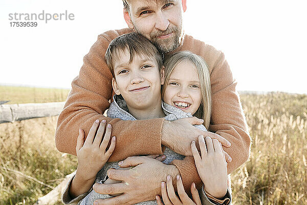 Father embracing smiling daughter and son on sunny day